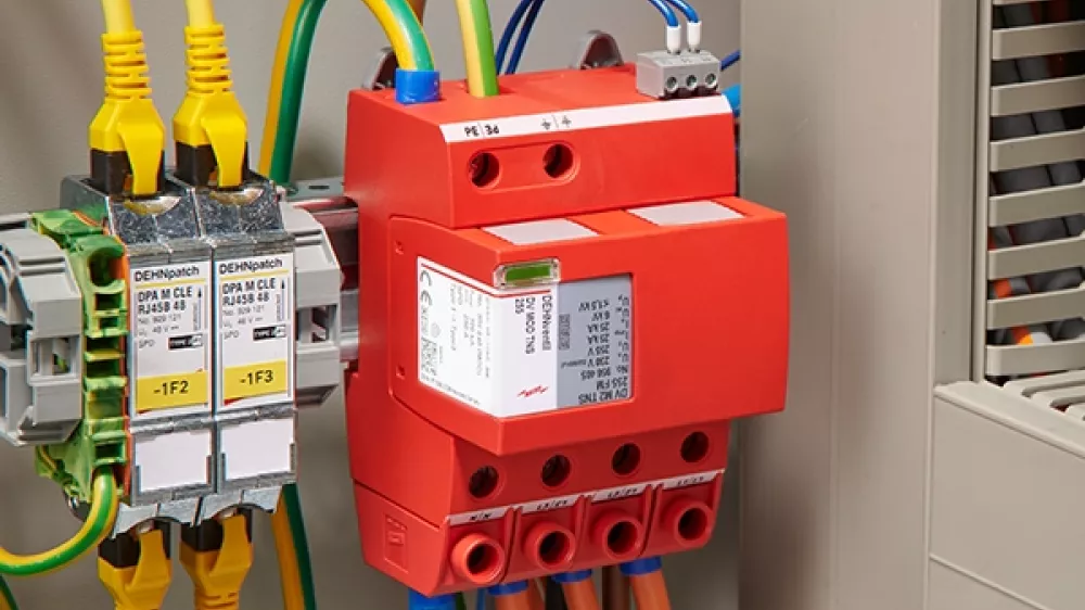 Descargador de sobretensiones rojo, montado y cableado junto a un armario eléctrico abierto.
