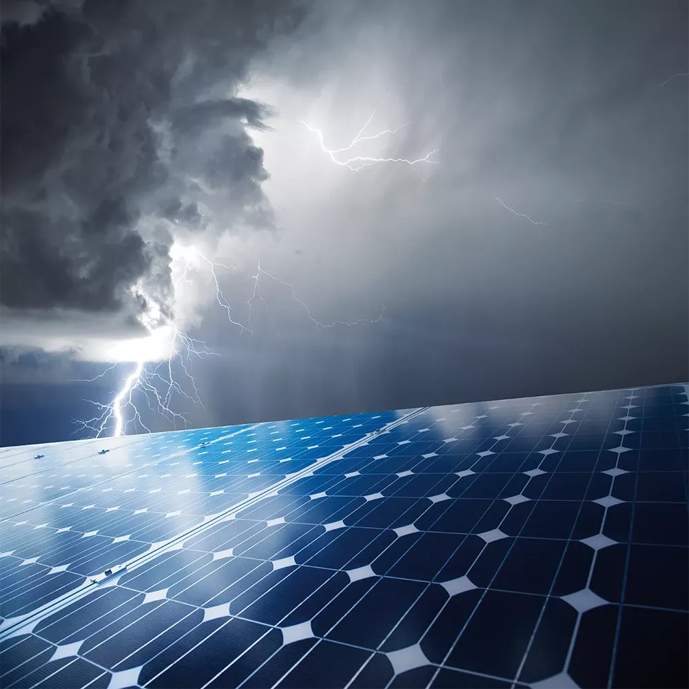 Paneles fotovoltaicos en primer plano. En el horizonte, amenazan nubes de tormenta de las que caen rayos.