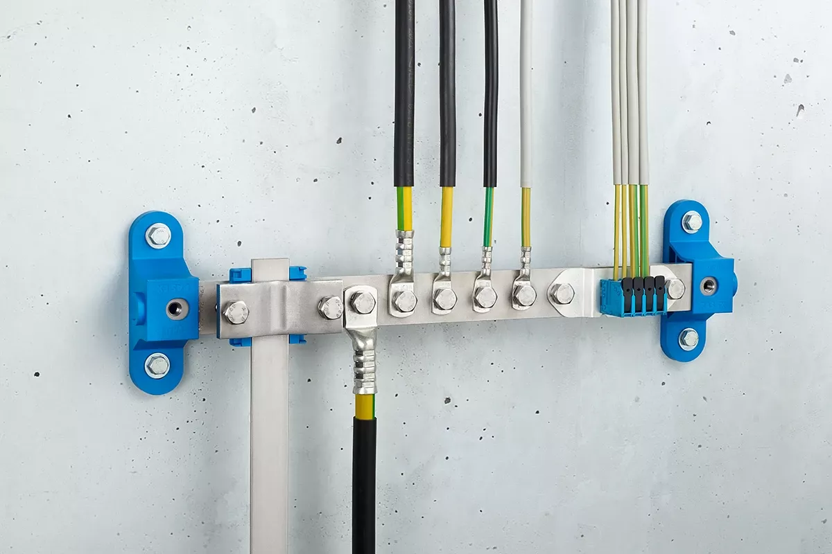 Barra de compensación de potencial con conexiones azules a la pared y cables negros, montada en una pared de hormigón gris.